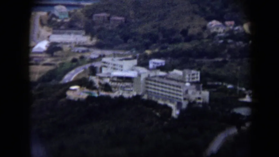 1959 Venezuela 8mm frame showing a large white hotel-like complex, winding roads, pools, and surrounding hills.