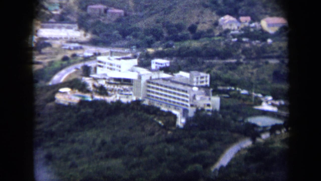 1959 Venezuela 8mm frame with a large white hillside hotel-like structure, access roads, pools, and nearby homes.