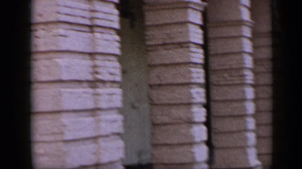 1959 Venezuela street footage showing textured stone columns and the edge of a hanging commercial sign.