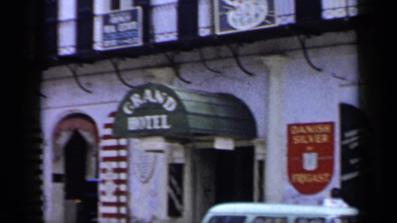 1959 Venezuela 8mm frame with angled handheld view of the Grand Hotel awning, adjacent signage, arched entry, and light-colored car.