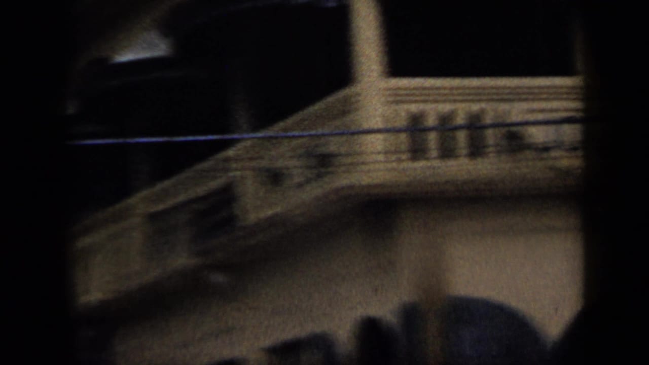 1959 Venezuela home-movie frame with a shadowed partial view of a pale building, balcony rail, and arched lower facade.