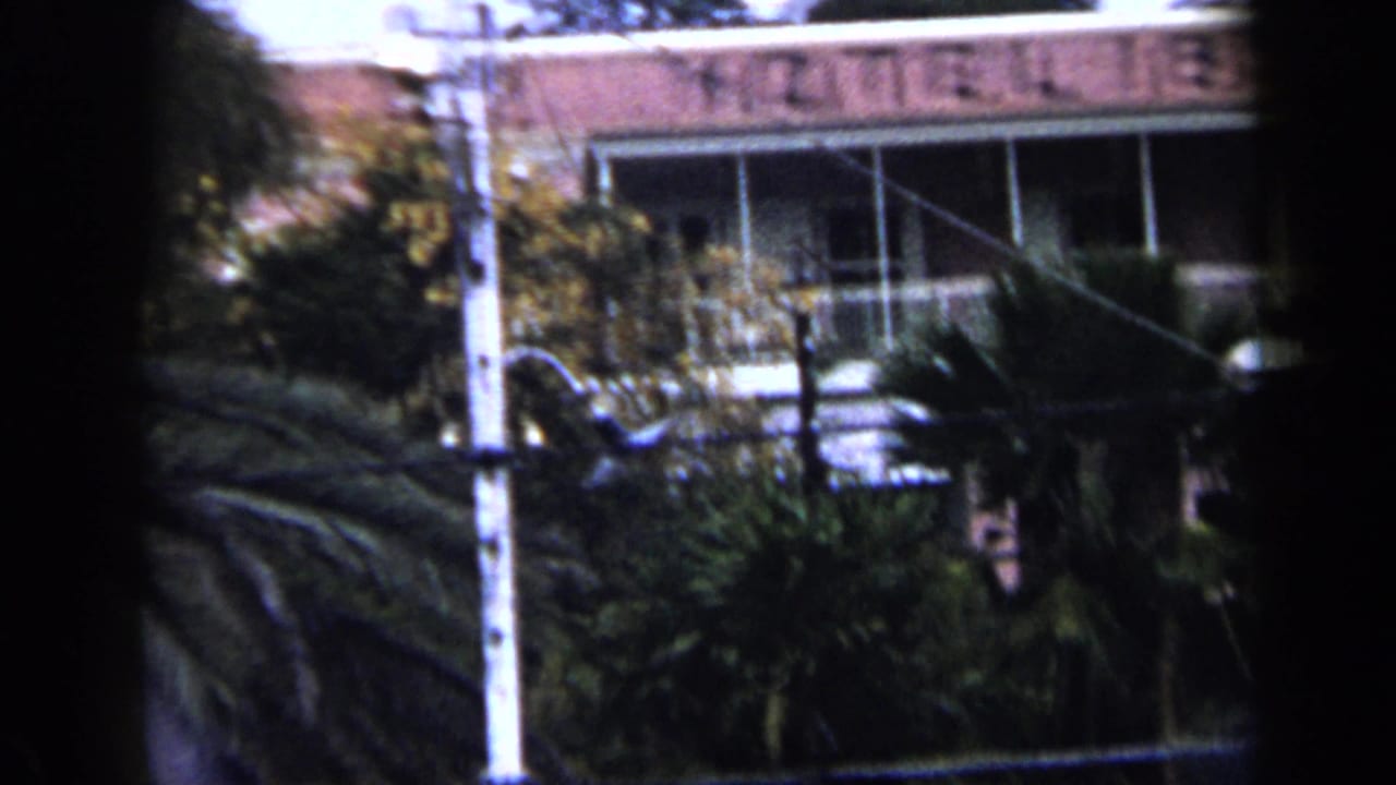 1959 Venezuela frame with the Hotel 1829 facade partly visible behind palms, balcony railings, a pole, and wires.