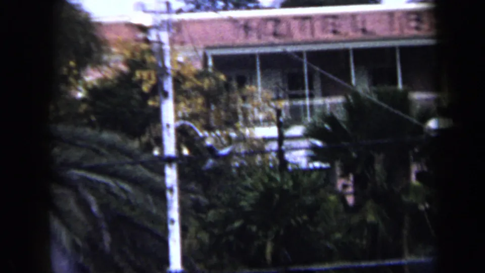 1959 Venezuela frame with the Hotel 1829 facade partly visible behind palms, balcony railings, a pole, and wires.