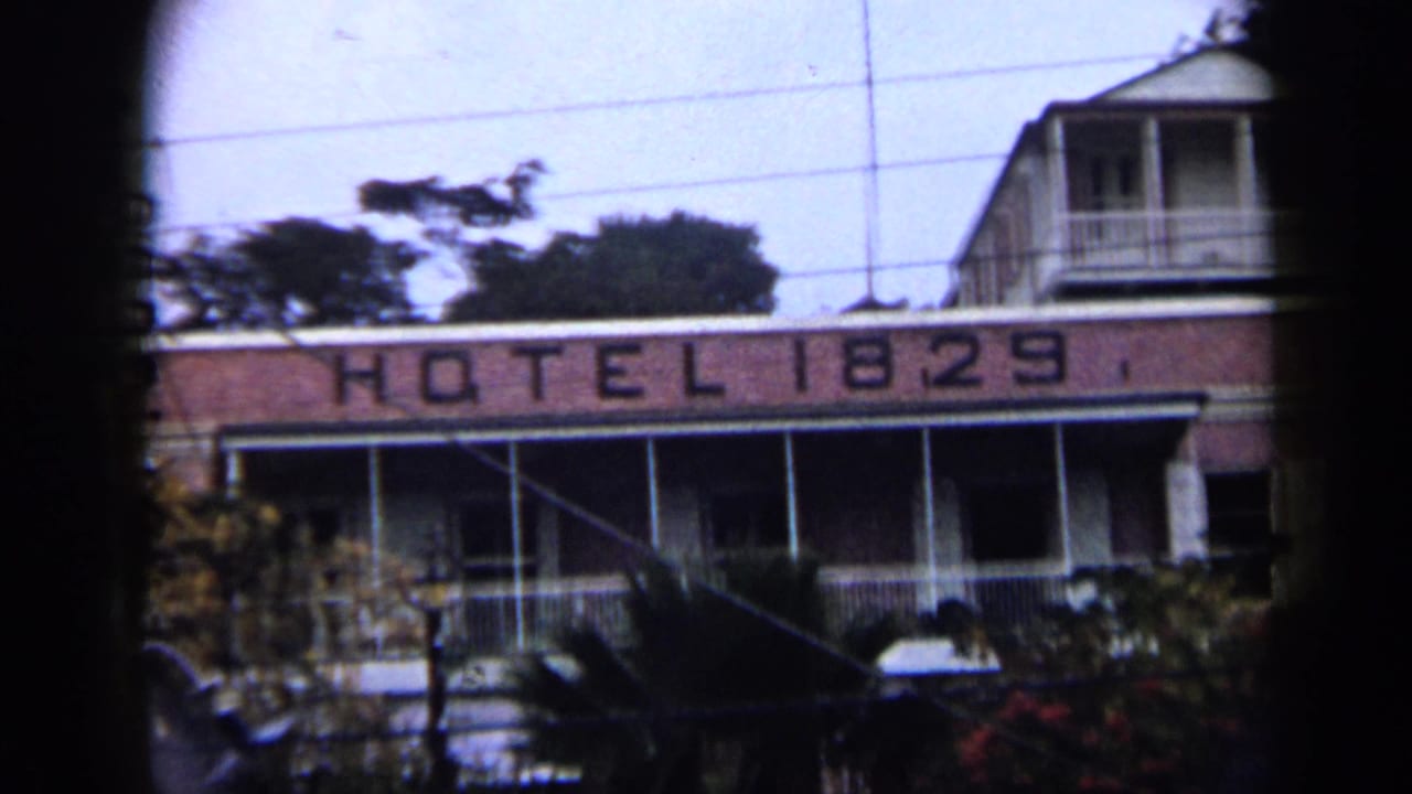 1959 Venezuela home-movie frame showing the Hotel 1829 sign, upper balcony, palm foliage, and overhead utility lines.