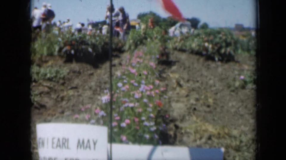 Wider 1961 Missouri garden view with rows of flowers, distant visitors, a small flag, and a foreground sign reading Earl May.