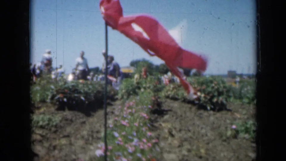 1961 Missouri 8mm frame with a windblown flag dominating the foreground and visitors behind flower beds.