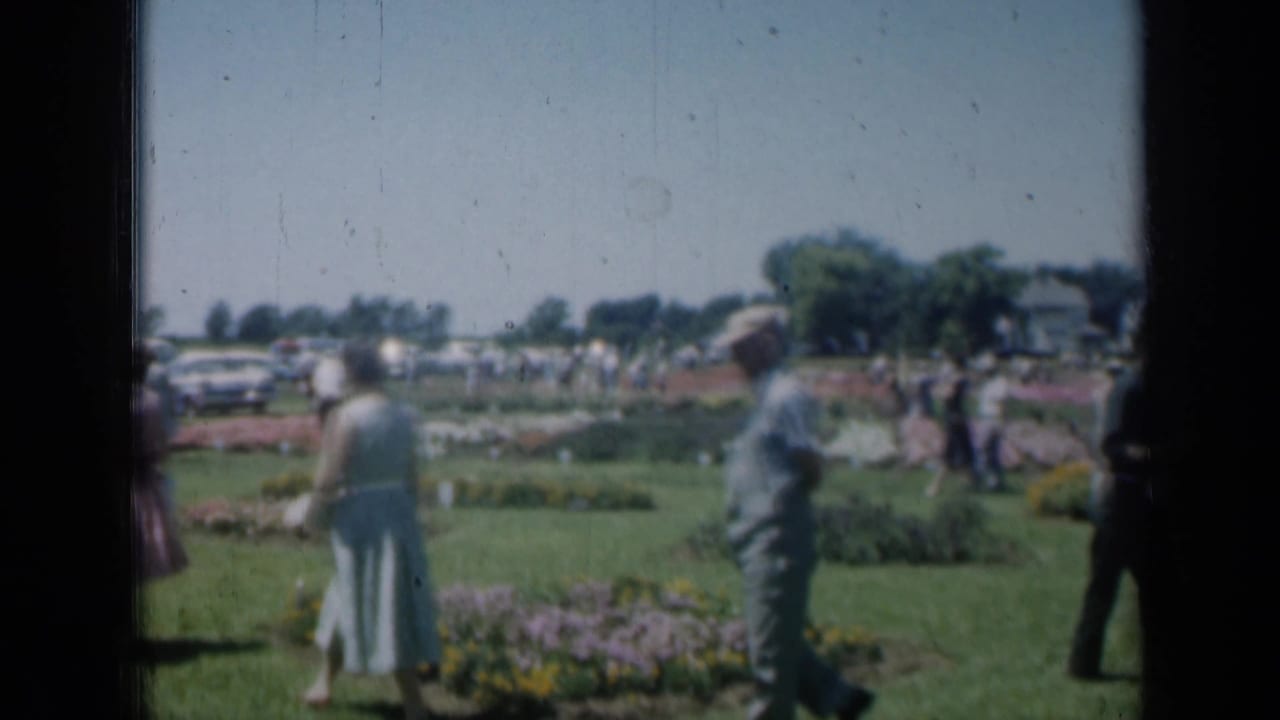 Adults stroll through a manicured garden with flower beds and lawns.
