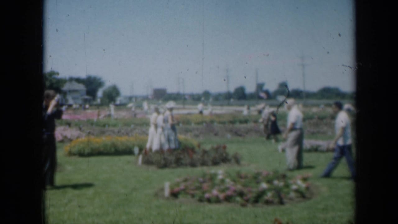 Adults walk across a public garden lawn with flower beds in the foreground.