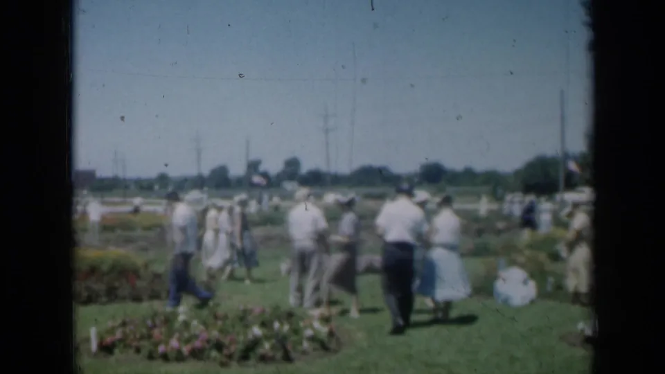 Adults stroll through a landscaped Missouri garden in 1961, framed by lawn, flower beds, and distant trees.