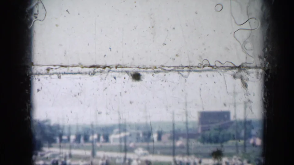 Soft 8mm Missouri frame with heavy dust and scratches over a roadside area, utility poles, trees, and a distant sign shape.
