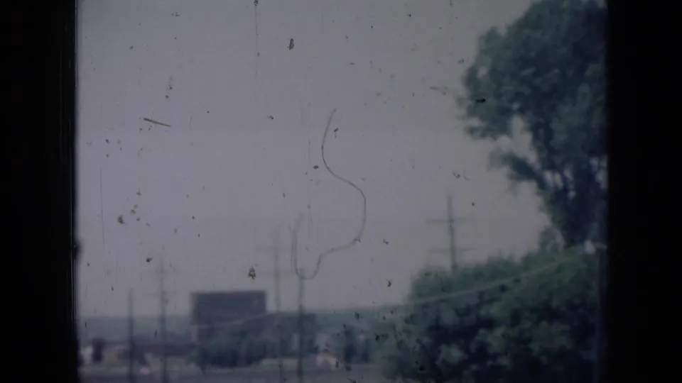 1961 Missouri 8mm frame showing a hazy roadside scene with trees, utility poles, distant shapes, and visible film dust.