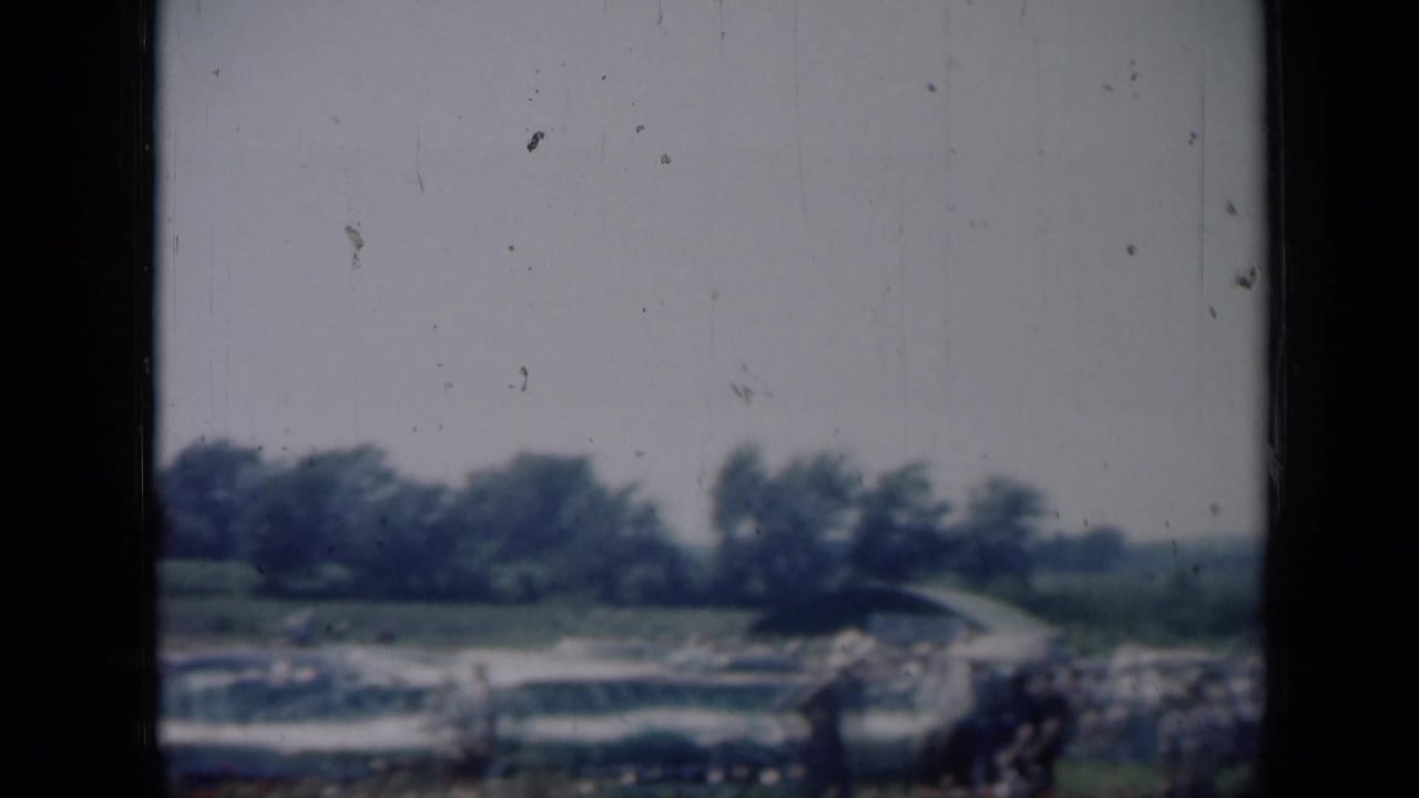 Distant view of a Missouri outdoor gathering with classic cars and people along the field edge.