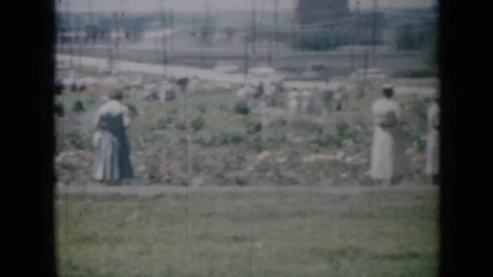 Soft 8mm view of women in long dresses near planted beds in a Missouri park or garden in 1961.