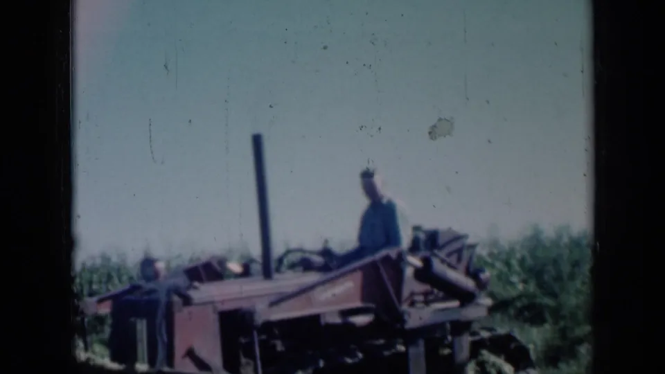 1961 Missouri frame showing a man silhouetted near heavy farm equipment at the edge of a crop field.