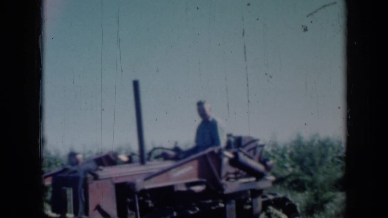 1961 Missouri farm scene with a man operating red machinery in an open field, seen through soft 8mm color footage.