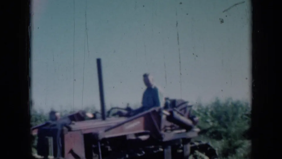1961 Missouri farm scene with a man operating red machinery in an open field, seen through soft 8mm color footage.