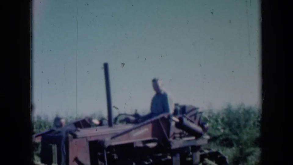 A 1961 Missouri 8mm frame shows a man on red farm equipment, with crop rows or vegetation and a washed bright sky behind him.