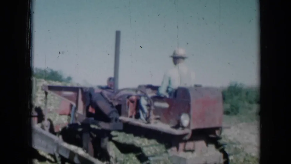1961 Missouri farm footage frame showing a seated farmer on a red tracked tractor under a clear sky.