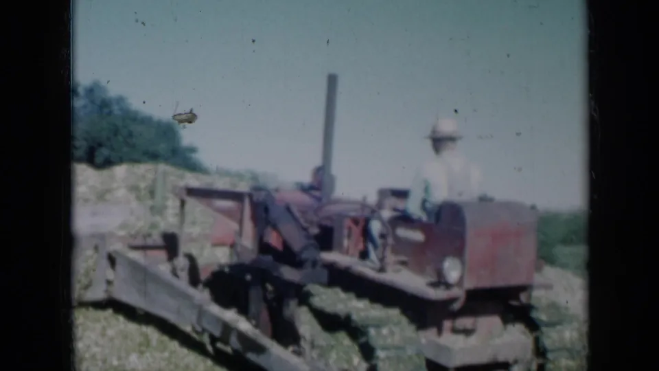 1961 Missouri 8mm frame of a farmer on a red tractor working near a low pile of cut crop material.