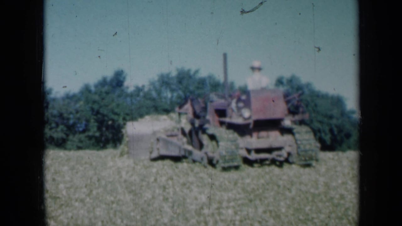 Tractor and operator continue pushing hay near a tree line.
