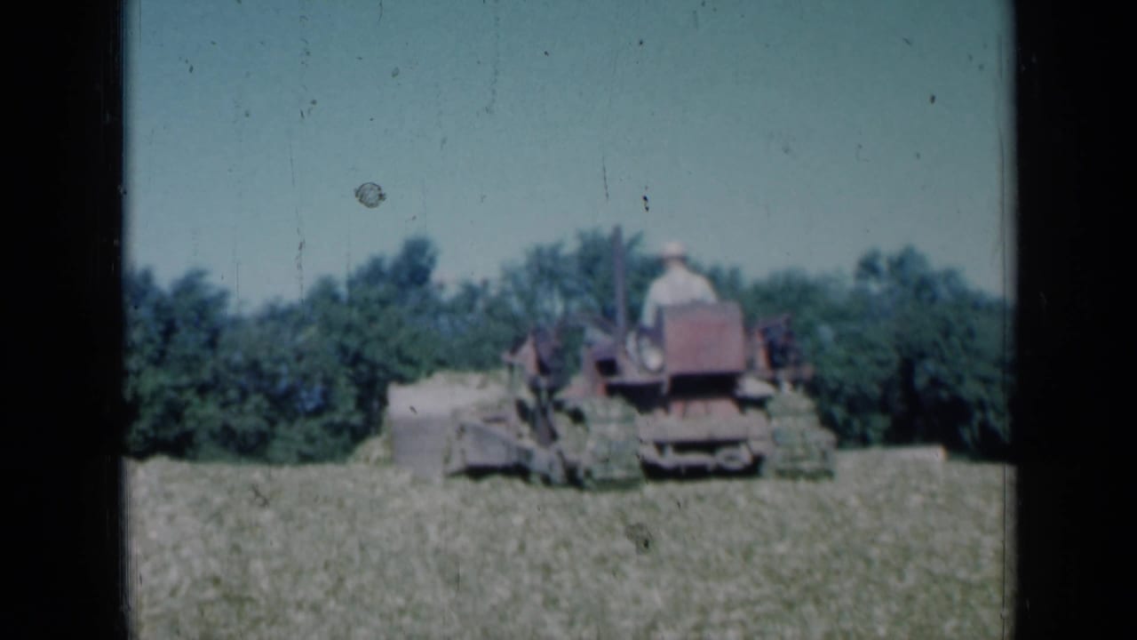 1961 Missouri 8mm frame showing a red tractor with a front blade moving through a grassy field near dense trees.