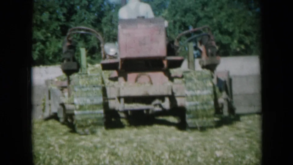 A red hay baler works through a sunlit Missouri field, with its operator mostly obscured behind the machine.