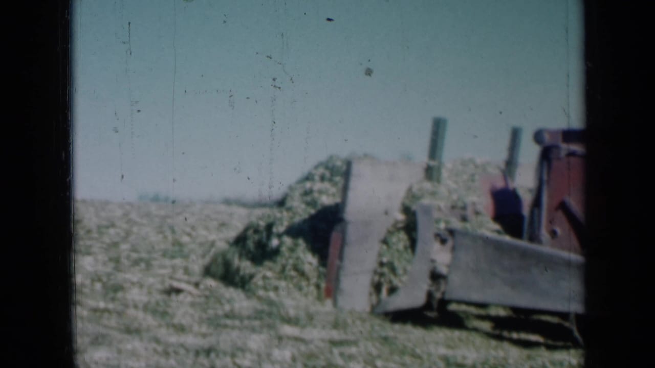 The 8mm frame shows the grader blade and red machinery pushing along a mound of vegetation in rural Missouri.