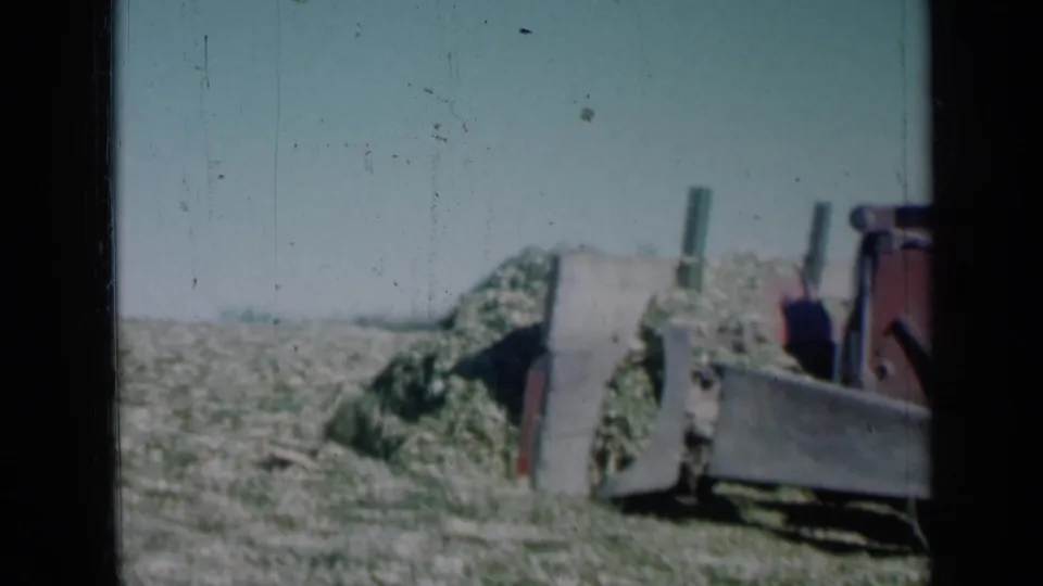 The 8mm frame shows the grader blade and red machinery pushing along a mound of vegetation in rural Missouri.