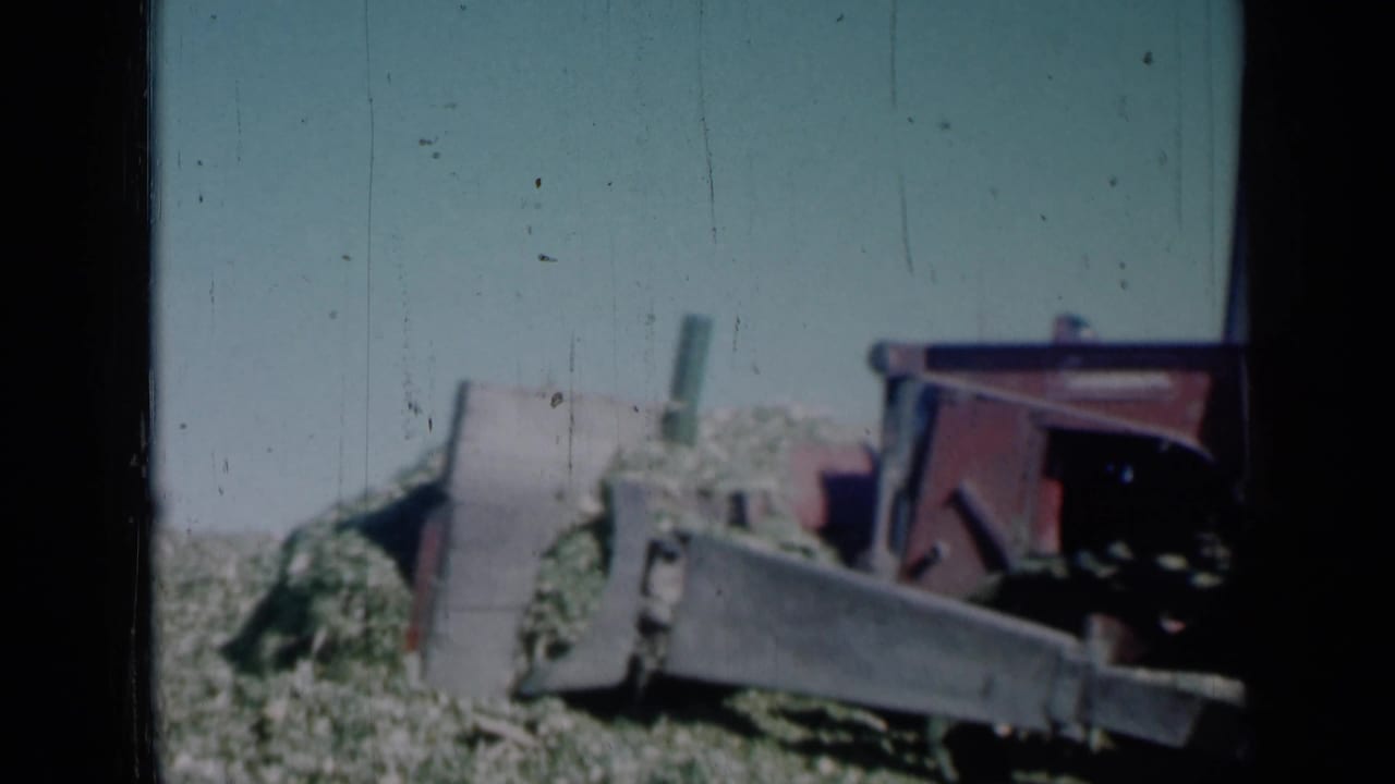 The final frame holds on the red grader and blade near piled vegetation, with the rural Missouri field stretching behind.