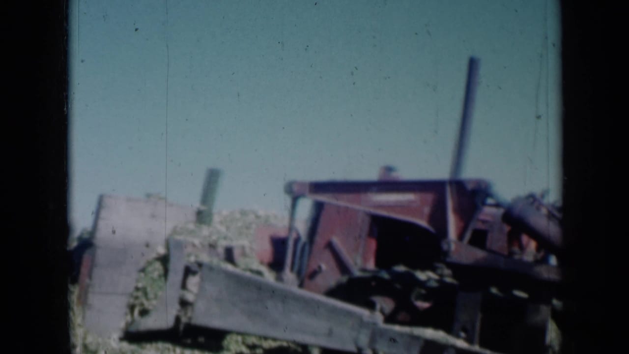 Red tractor entering a crop field under a clear sky, with a seated operator partly visible.