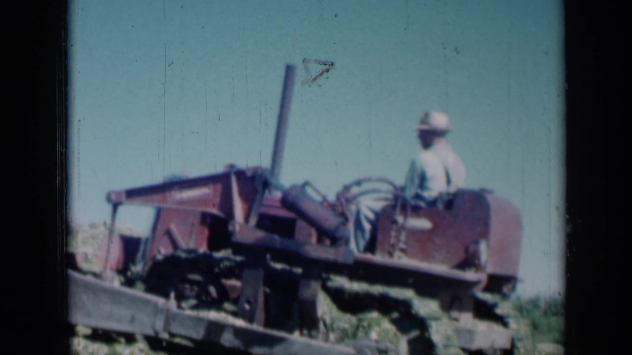 Side view of the tractor operator riding through a harvested Missouri field, with soft 8mm color and visible frame wear.