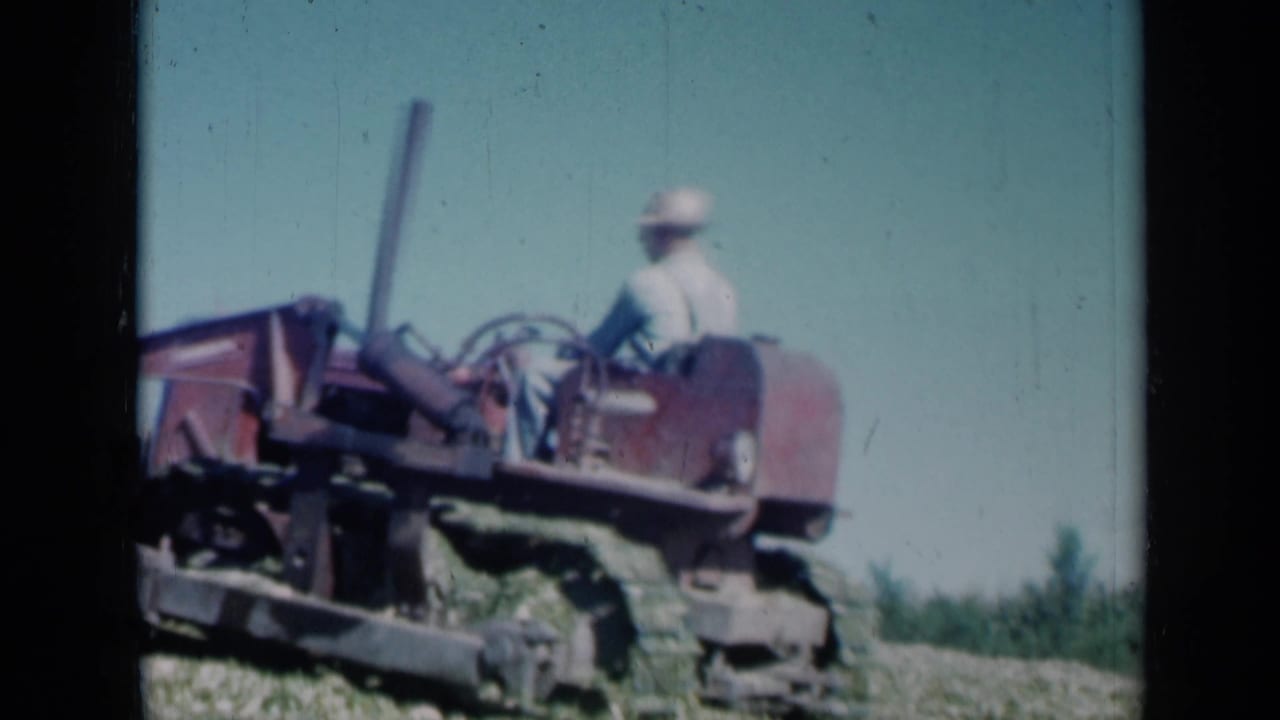 End frame of a man on a red tractor crossing a Missouri field, with open sky and soft 8mm home-movie texture.