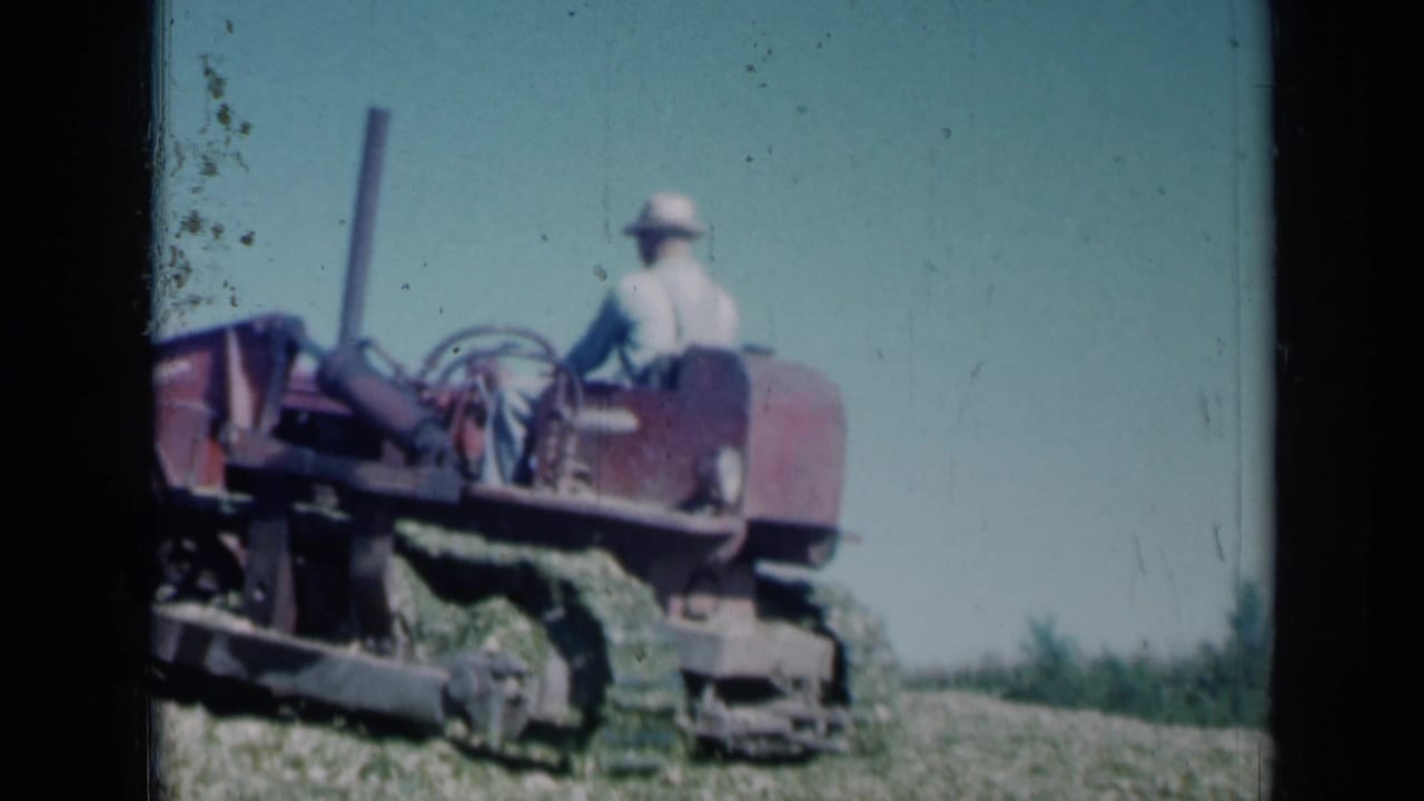 1961 Missouri home-movie frame showing a man on a red tractor in a field under a bright blue sky.