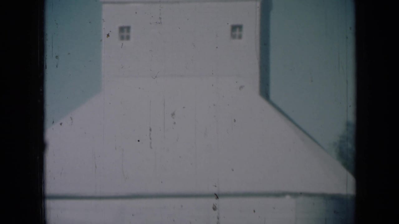 Large white farm storage building in 1961 Missouri footage, framed close with small upper windows visible.