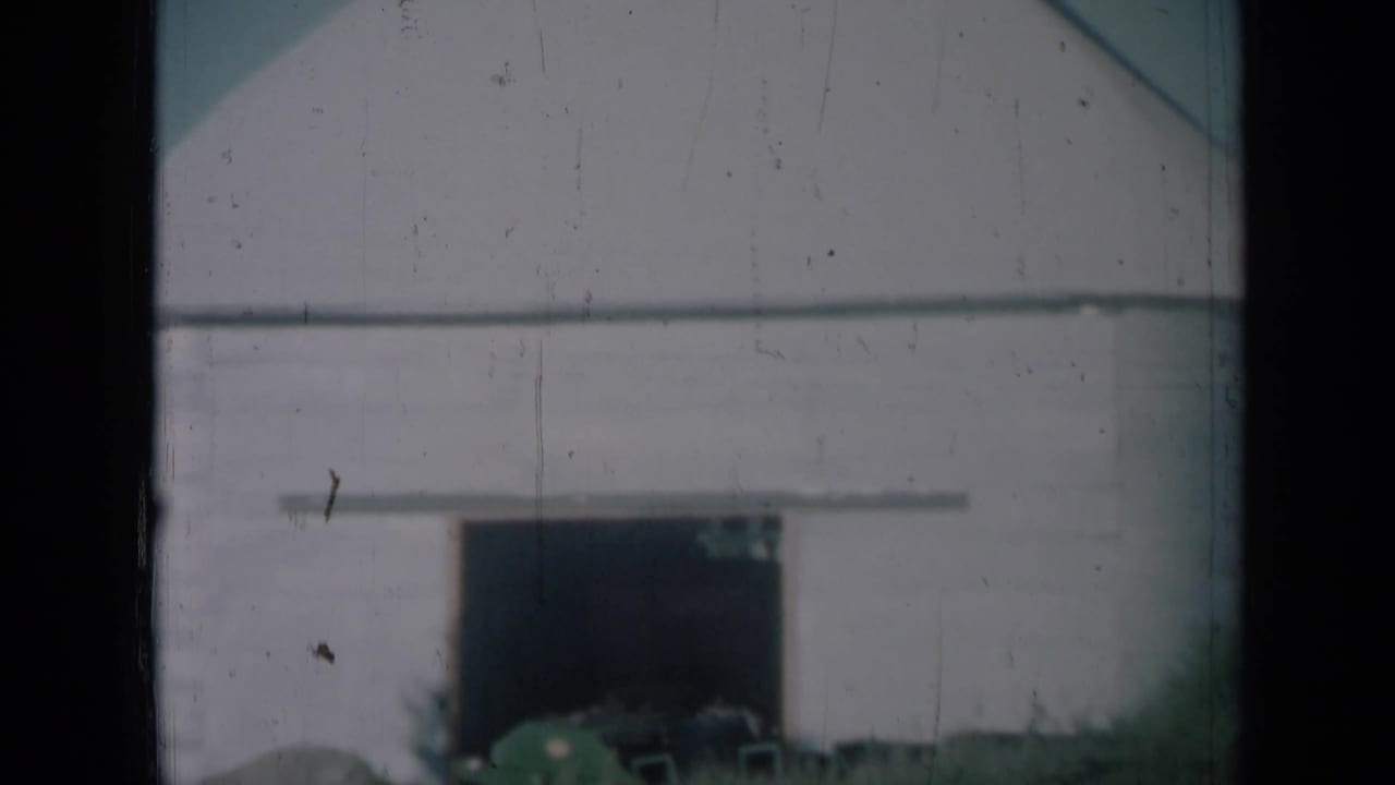 1961 Missouri home-movie view of a white storage building with a dark doorway and grass in the foreground.