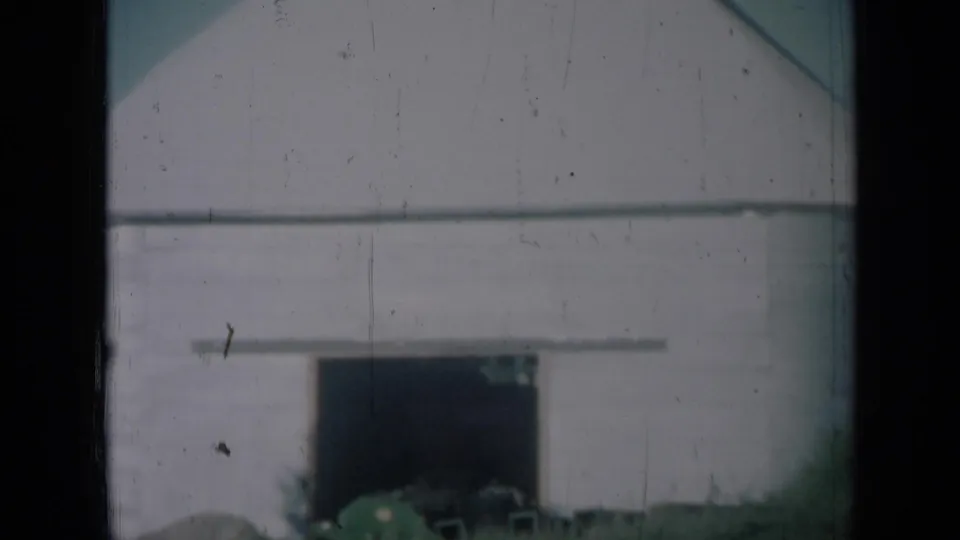 1961 Missouri home-movie view of a white storage building with a dark doorway and grass in the foreground.