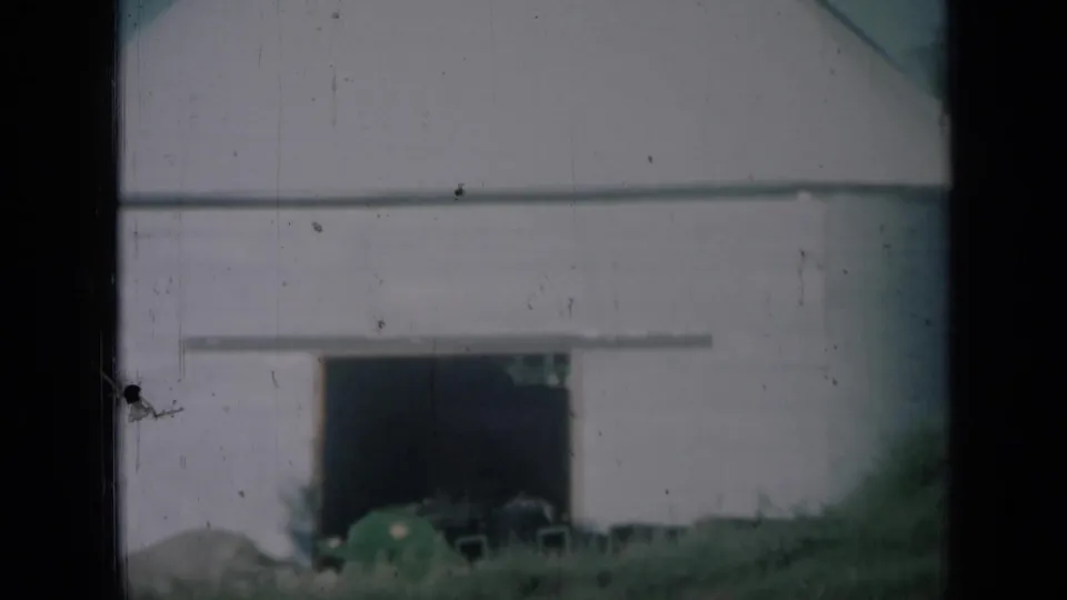 1961 Missouri farm footage showing a pale barn-like building, open doorway, grassy foreground, and dark 8mm frame borders.