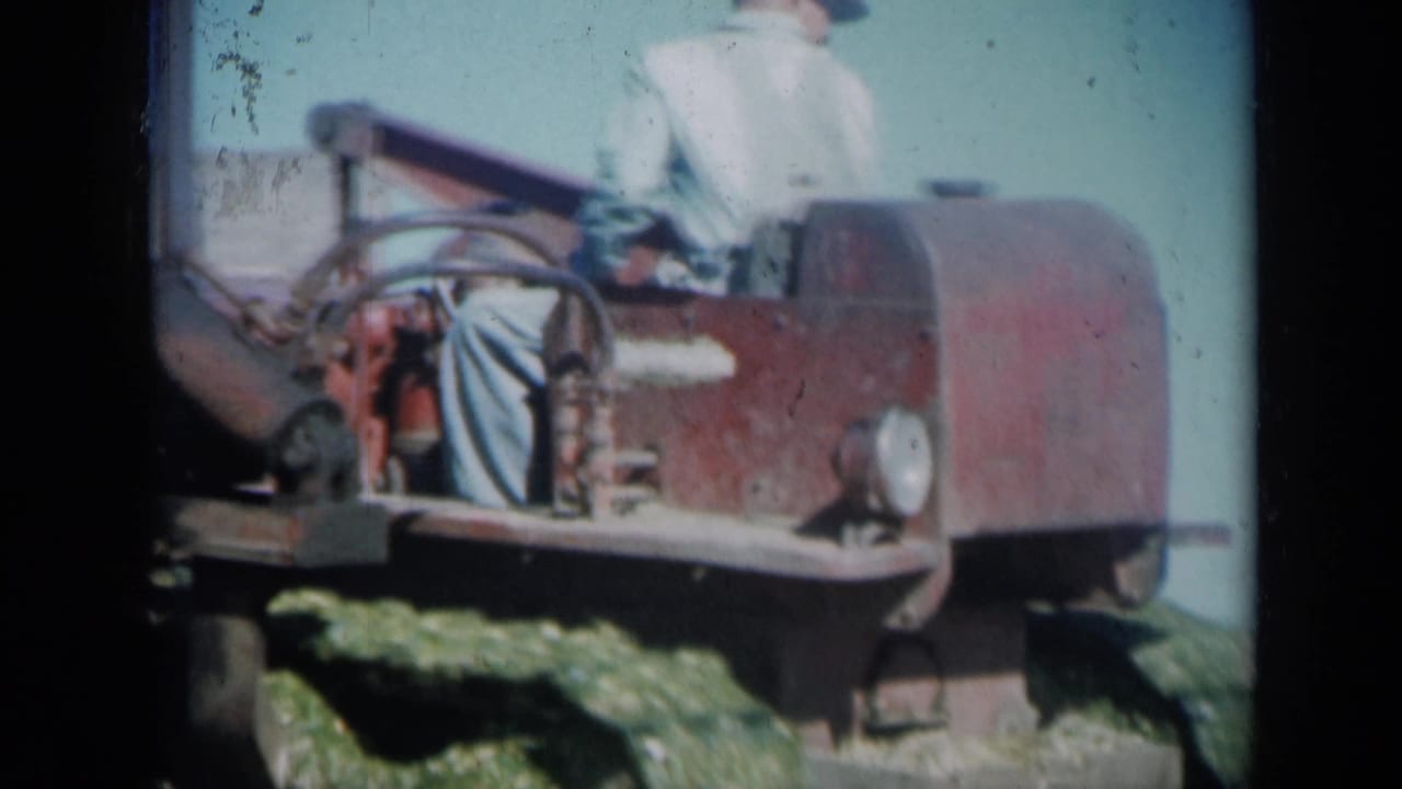 A red tracked tractor passes close in the frame, with an adult operator partly visible in 1961 Missouri farm home-movie footage.