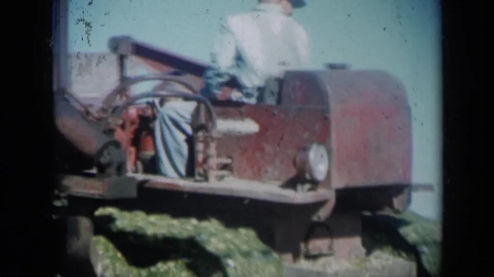 A red tracked tractor passes close in the frame, with an adult operator partly visible in 1961 Missouri farm home-movie footage.