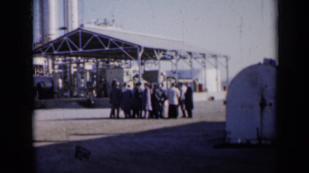 Small group standing on pavement before a large metal industrial structure.