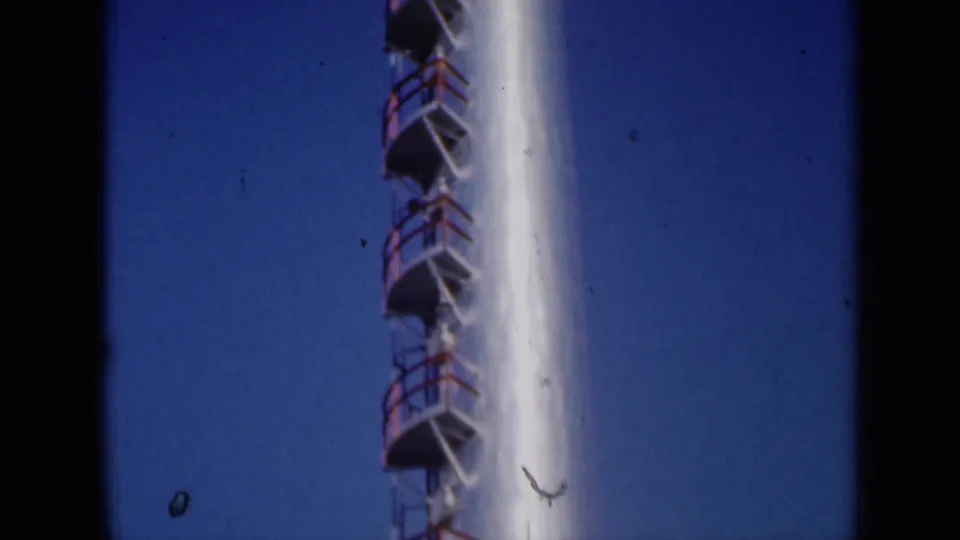 1961 Missouri 8mm frame of the lower visible section of a white industrial stack with red ladder platforms.