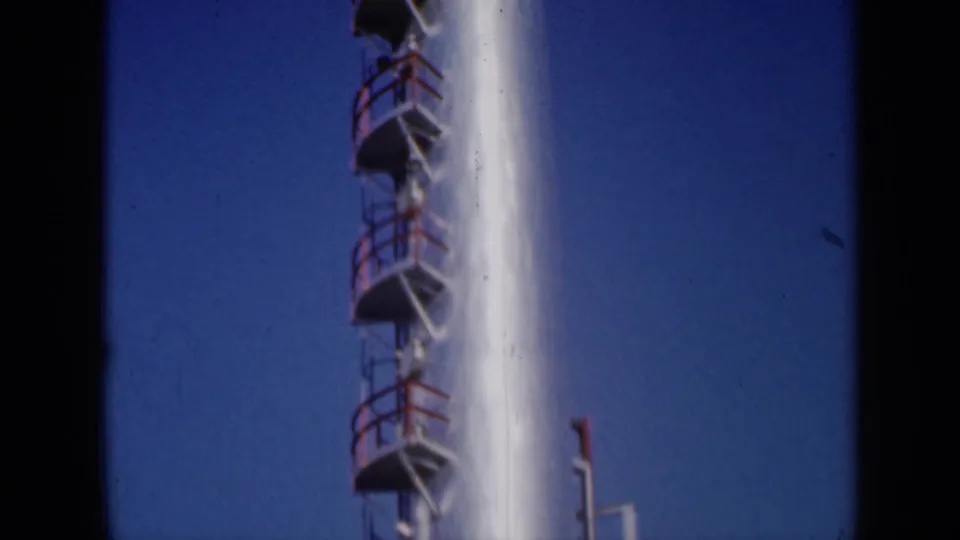 1961 Missouri 8mm view of a white industrial stack, red ladder platforms, and a small pipe near the lower edge.