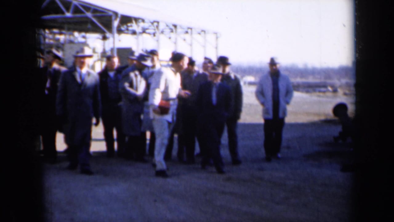 Group of men in suits and hats standing near an industrial structure outdoors.