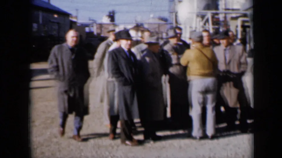 At a Missouri industrial facility, one man walks by while others in coats and hats remain gathered in conversation.