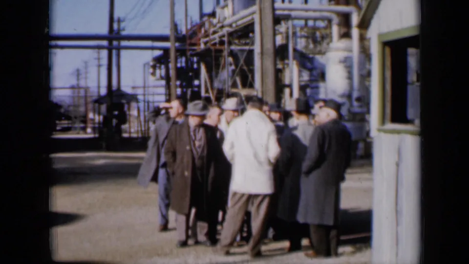 A home-movie view of men in overcoats and hats gathered near pipes and metal structures at a 1961 Missouri industrial facility.