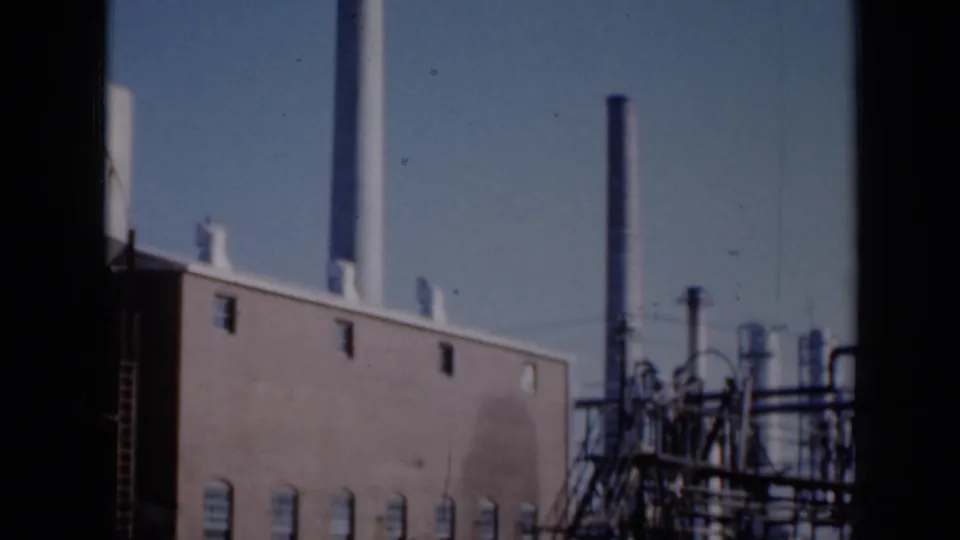 1961 Missouri 8mm frame showing a brick industrial plant exterior with tall stacks, pipes and rooftop details against clear sky.