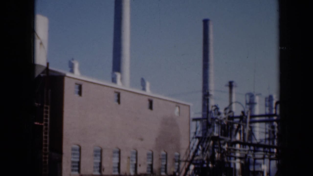 Brick factory building with smokestack and industrial pipework under a blue sky.