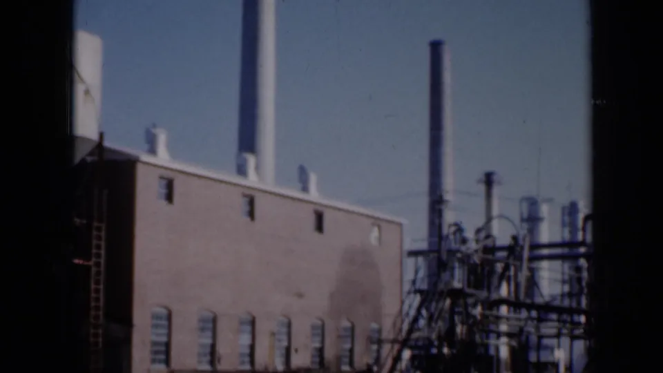 1961 Missouri 8mm frame showing a brick industrial building, tall stack, and metal pipe infrastructure under clear sky.