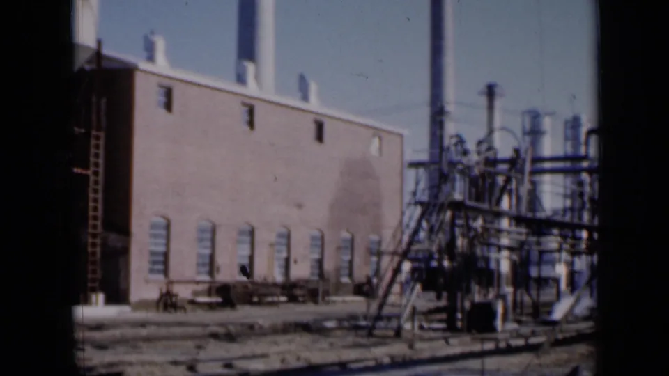 1961 Missouri 8mm view of a brick factory side with arched windows, ladders, pipework, and exterior industrial equipment.