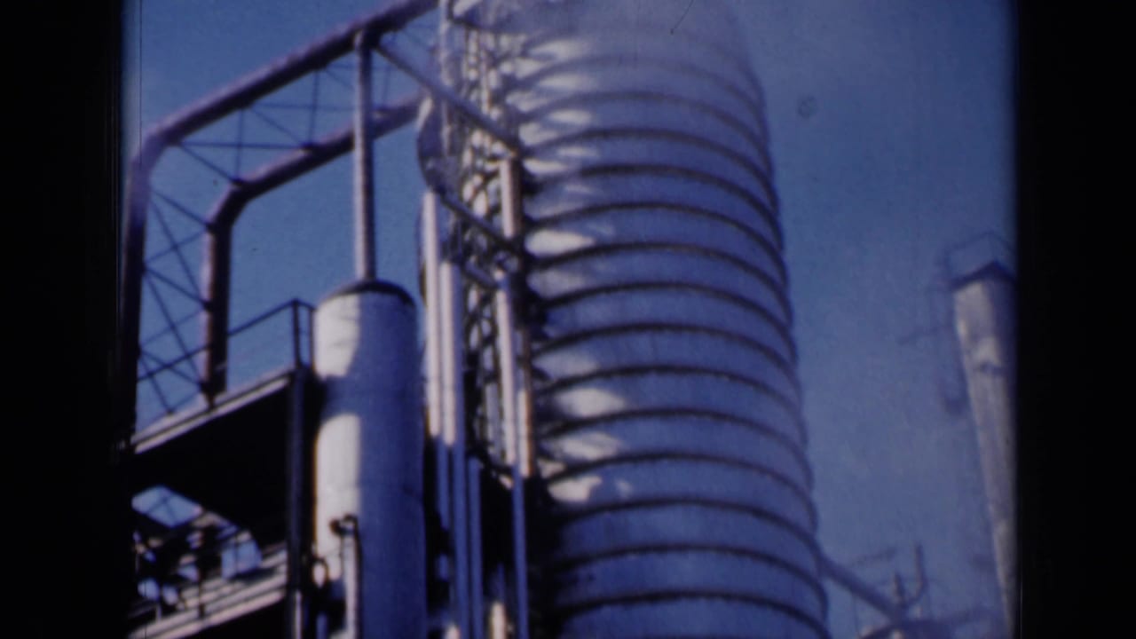 Industrial tower and adjacent pipes with metal walkways silhouetted against the sky.